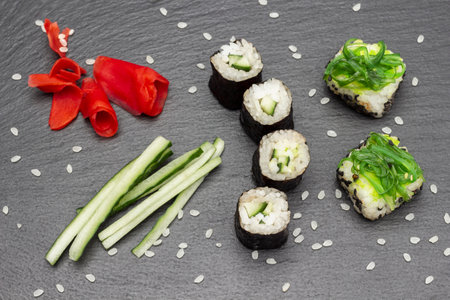 Sushi nori and sushi with seaweed, sliced cucumber and pickled ginger. flat lay. Black stone background.の写真素材