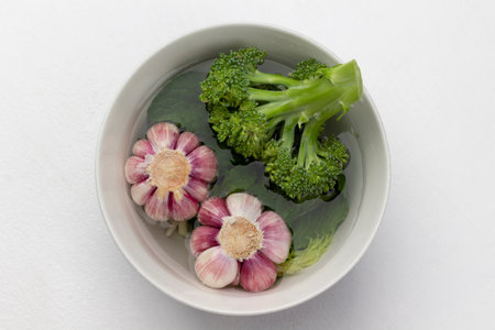 Garlic and broccoli in a bowl of water. food still life. copyspace. flat lay. white background.の写真素材