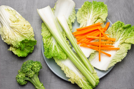 Cabbage leaves, celery stalks and sliced carrots on gray plate. Broccoli and Chinese cabbage on table. flat lay. gray background.の写真素材