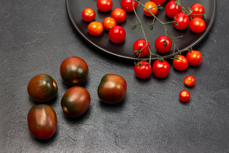 Sprig of cherry tomatoes on black plate. Red tomatoes on the table. copyspace. flat lay. Black background.の写真素材