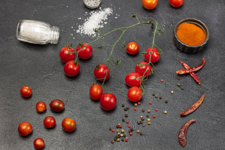 Sprig of cherry tomato. Salt shaker, allspice, red pepper in bowl on table. Top view. Black background.の写真素材
