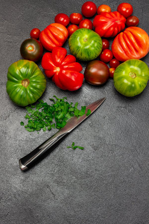 Different varieties of red and green tomatoes. Chopped parsley and knife. copyspace. flat lay. Black background.の写真素材