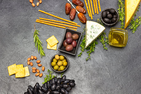 Appetizer for an aperitif with olives and cheese, grapes and dates, baguette and crackers, nuts and thyme sprigs. copyspace. flat lay. Black background.の写真素材