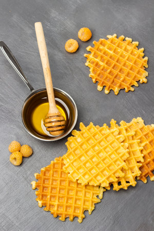 Viennese waffles and yellow raspberries on table. Metal bowl with honey and wooden honey stick. flat lay. gray background.の写真素材