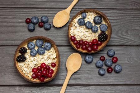 Whole oats, blueberries and cranberries in coconut bowls. Two wooden spoons and berries on the table. flat lay. Dark wooden background.の写真素材