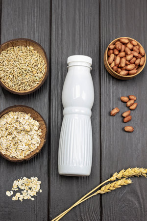 Ingredients for breakfast. Milk bottle and uncooked oatmeal. Sprigs of wheat and grains of wheat in bowl. Nuts in bowl and on table. flat lay. Dark wooden background.の写真素材