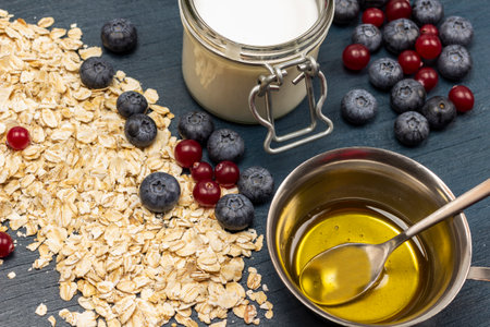 Whole oatmeal, blueberries and cranberries on table. Yogurt in jar, honey in metal bowl. top view. blue background.の写真素材