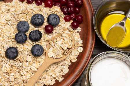 Uncooked oatmeal with berries. Yogurt in jar, honey in metal bowl. Part of the frame. close up.の写真素材