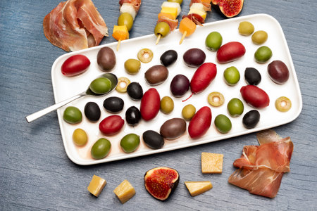 Jamon, cheese, figs and skewers with cheese, olives and jamon on table. Olives of various varieties on plate. flat lay. blue background.の写真素材