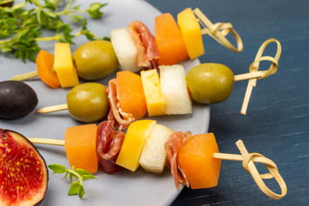 Skewers with cheese, olives and jamon on gray plate. close up. blue background.の写真素材