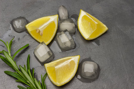 Lemon slices, rosemary sprig and melted ice on the table. Flat lay.Grey background.の写真素材