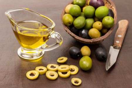 Green olives cut into rings and knife on table. Olives of various varieties in coconut shell. Olive oil in bowl. top view. brown background.の写真素材