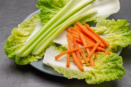 Lettuce leaves, celery stalks and sliced carrots on a gray plate. top view. gray background.の写真素材