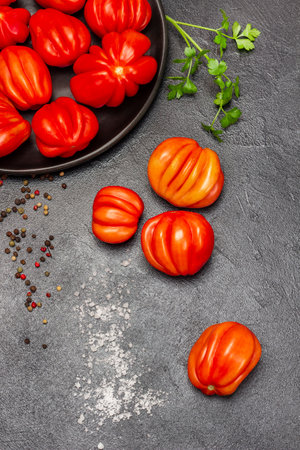 Red tomatoes on plate and table. Sprig of parsley, allspice and salt. top view. Black background.の写真素材