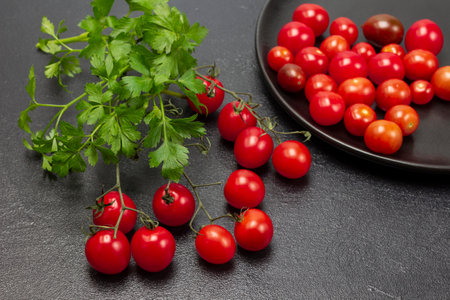 Sprig of parsley and sprig of red cherry tomatoes on table. Small red tomatoes on black plate. top view. black backgroundの写真素材