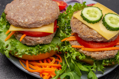 Two cheeseburgers with greens, chopped onion and carrots on gray plate. close up. Black background.の写真素材