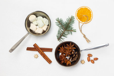 Cinnamon sticks, sprig of spruce and dry orange on string. Marshmallow and star anise in metal bowls. flat lay. white background.の写真素材