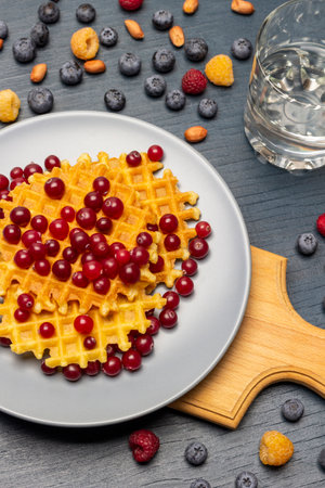 Cranberries and waffles on a gray plate. Glass of water and berries on the table. flat lay. gray background.の写真素材