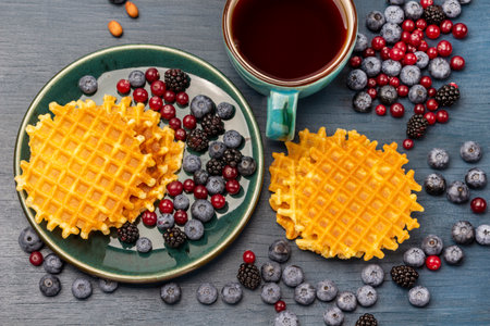 Blueberries, blackberries, cranberries and waffles on the table and on a plate. A cup of coffee in a mug. flat lay. gray background.の写真素材