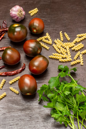 Brown tomatoes, parsley sprigs, spices and pasta. top view. brown background.の写真素材