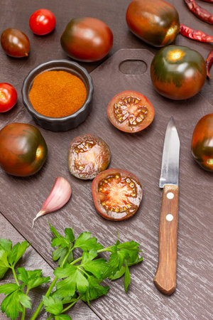 Knife and halves of a tomato. Whole tomatoes on table, paprika in bowl. top view. brown background.の写真素材