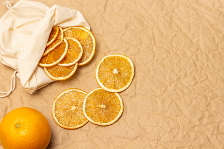 Slices of dried orange in a fabric bag. Fresh, whole orange. copyspace. flat lay. Beige paper background.の写真素材