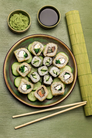 Sushi and sliced cucumbers on a green plate. Wasabi and soy sauce in bowls. Bamboo sushi mat and chopsticks. green background.の写真素材