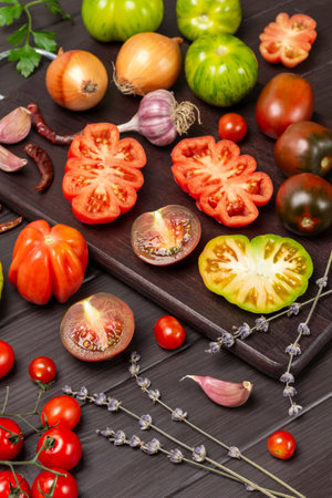 Tomatoes of different varieties on cutting board. Garlic and lavender sprigs on table. top view. Dark wooden background.の写真素材