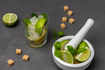 Glass with lime, mint and ice. Lime and mint in a mortar. Half a lime and pieces of brown sugar on the table. top view. gray background.の写真素材