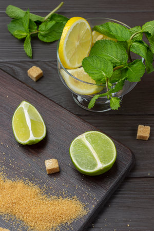 Fresh lemon and mint in a glass bowl. Two fresh lime halves and brown sugar. top view. Dark wooden background.の写真素材
