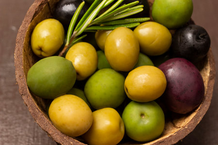 Multi-colored olives and a sprig of rosemary in a coconut shell. close up.の写真素材