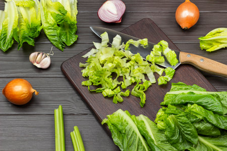 Chopped lettuce leaves and knife on cutting board. Vegetables on table. top view. Dark wooden background.の写真素材