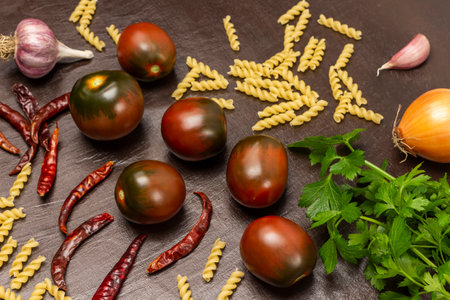Brown tomatoes, parsley, pasta and dry red pepper pods on the table. top view. brown background.の写真素材
