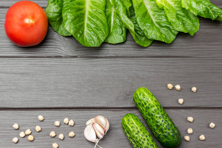 Cucumbers, garlic and chickpeas. Tomato and lettuce leaves. flat lay. copyspace. Dark wooden background.の写真素材