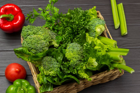 Green vegetables in a wicker basket. Tomatoes and peppers on the table. top view. Dark wooden background.の写真素材