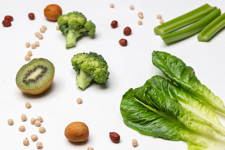 Lettuce leaves, celery stalks, half a kiwi and nuts on a white background. top viewの写真素材