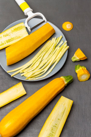 Sliced zucchini and vegetable peeler on a gray plate. Zucchini on the table. flat lay. gray background.の写真素材