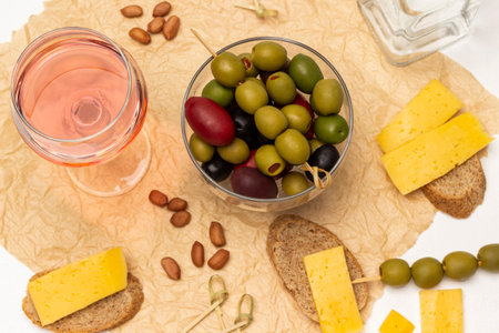 Different varieties of olives in a glass bowl. A glass of rose wine, bread with cheese on paper. flat lay. white background.の写真素材