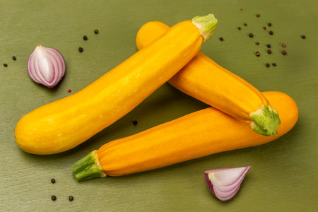 Yellow zucchini and blue onion halves, allspice. top view. green background.の写真素材