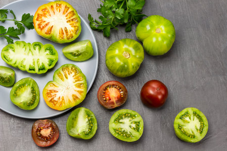 Halves of green tomatoes on a gray plate. Whole tomatoes and tomato halves on the table. Parsley springs. gray background.の写真素材