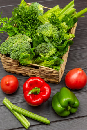 Tomatoes and peppers on the table. Lettuce, broccoli and celery stalks in a wicker basket. top view. Dark wooden background.の写真素材