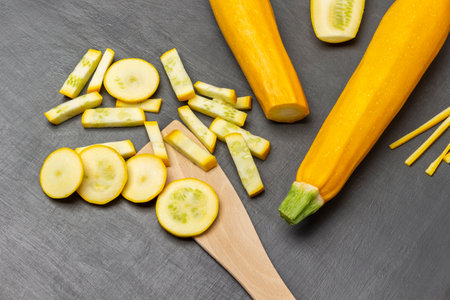 Sliced yellow zucchini and a wooden spatula. Whole zucchini. flat lay. gray background.の写真素材