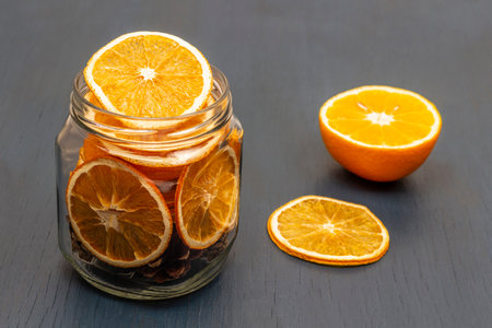 Half a fresh orange on the table. Dry orange slices and fir cones in a jar. gray background.の写真素材