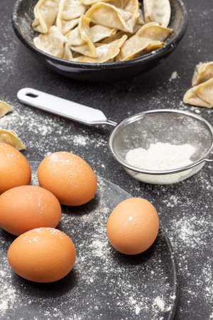 Eggs on plate and flour in sieve. Raw gyoza in bowl. top view. Black background.の写真素材