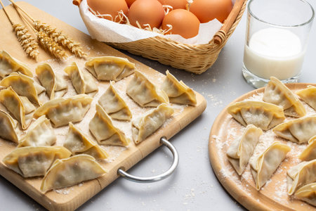 Raw gyoza dumplings on a cutting board. Eggs in wicker basket and glass of milk. top view. gray background.の写真素材