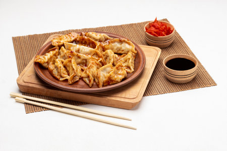 Gyoza dumplings on ceramic plate. Chopsticks on table. Two bowls with soy sauce and pickled ginger. top view. white backgroundの写真素材