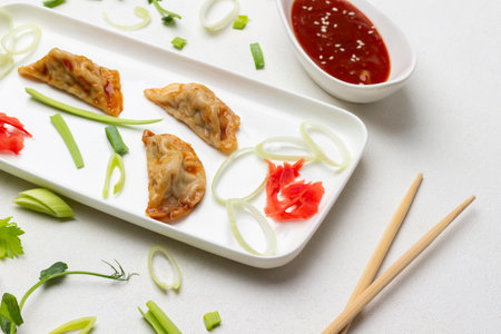 Chopsticks on table. Gyoza dumplings and chopped leek on white plate. Bowl with tomato sauce. top view. white backgroundの写真素材
