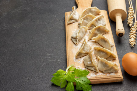 Raw gyoza dumplings on cutting board. Egg and rolling pin on table. copyspace. top view. black backgroundの写真素材