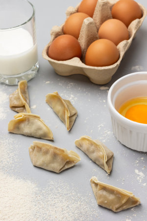 Flour and raw gyoza dumplings on table. Eggs in cardboard tray. Glass of milk and yolk in bowl. top view. gray backgroundの写真素材