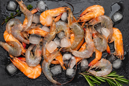 Raw shrimp and ice on wet stone surface. Sprig of rosemary. flat lay. black backgroundの写真素材